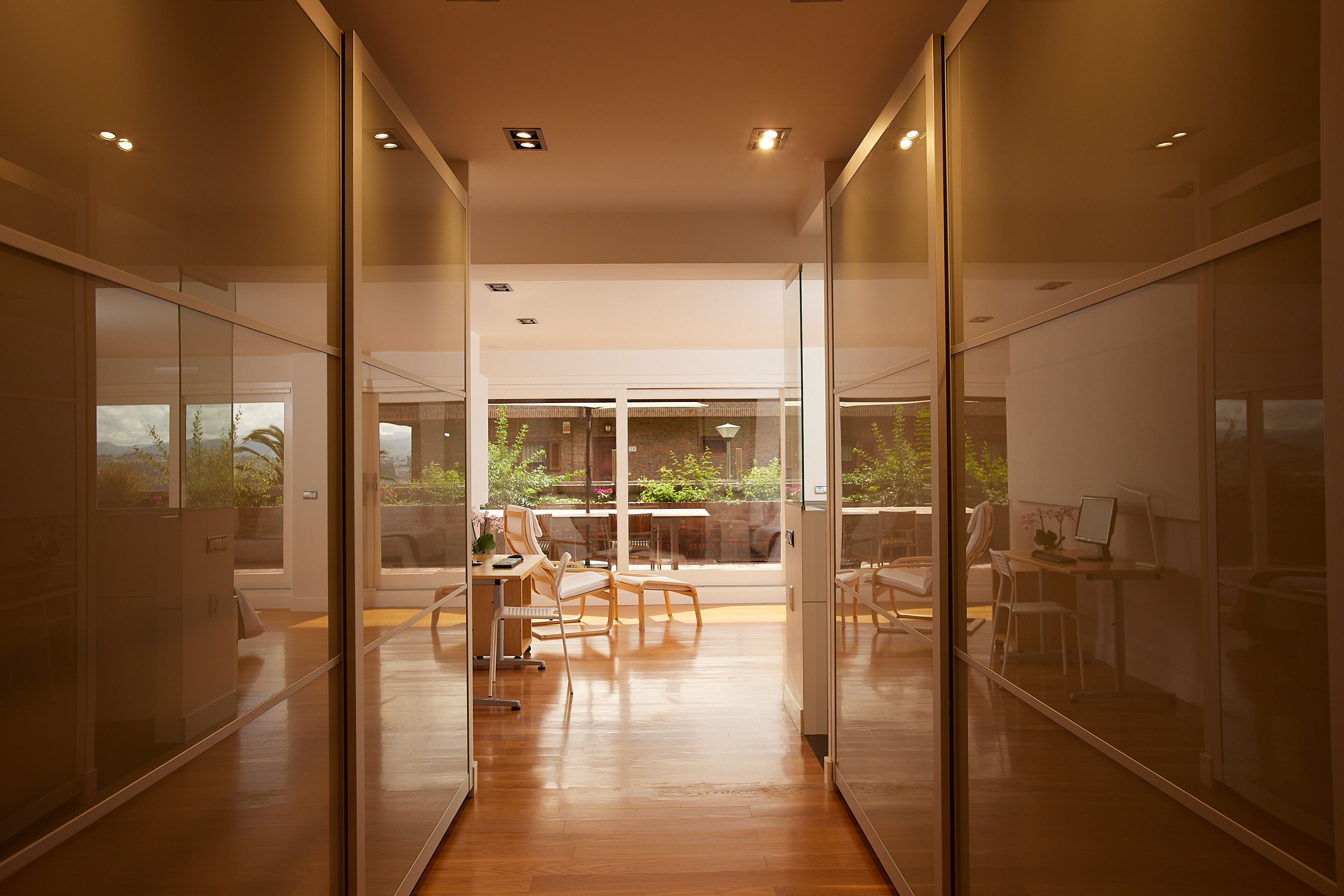 A modern interior with glass partitions, wooden flooring, and a dining area with chairs and tables.