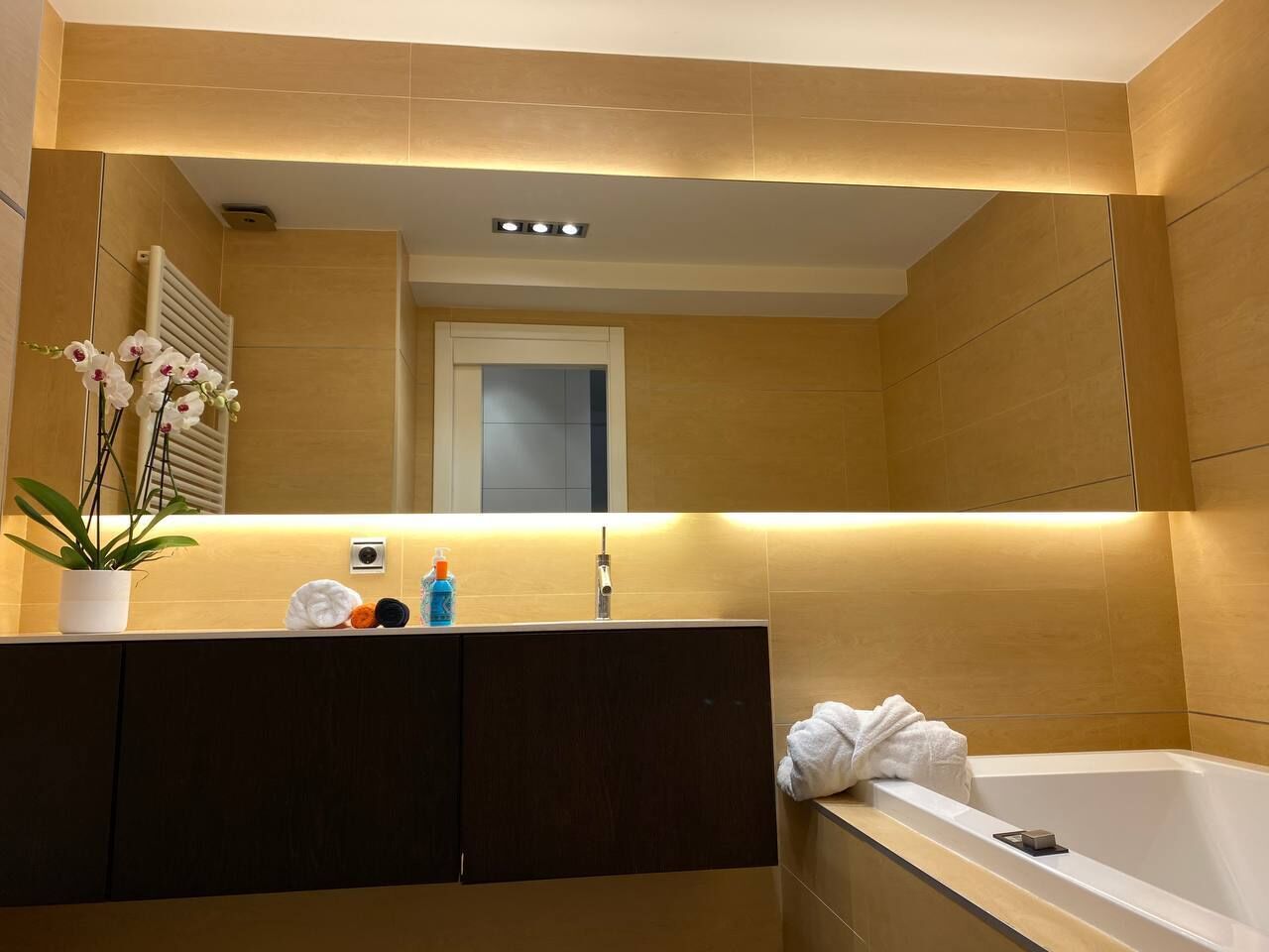 Un bagno moderno con un mobile bagno in legno, una vasca da bagno bianca e uno specchio sopra il lavandino.