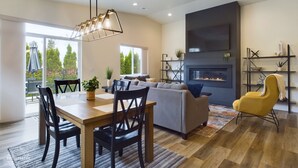 Een moderne woonkamer met een open haard, een eethoek met een houten tafel en stoelen, en een bank.