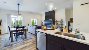 Een moderne keuken met een vaatwasser, een eethoek met tafel en stoelen, en een woonkamer met een bank en een open haard.