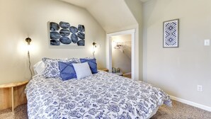Une chambre dotée d’un grand lit, de deux lampes fixées au mur, d’une œuvre d’art décorative et d’une porte donnant sur un couloir.