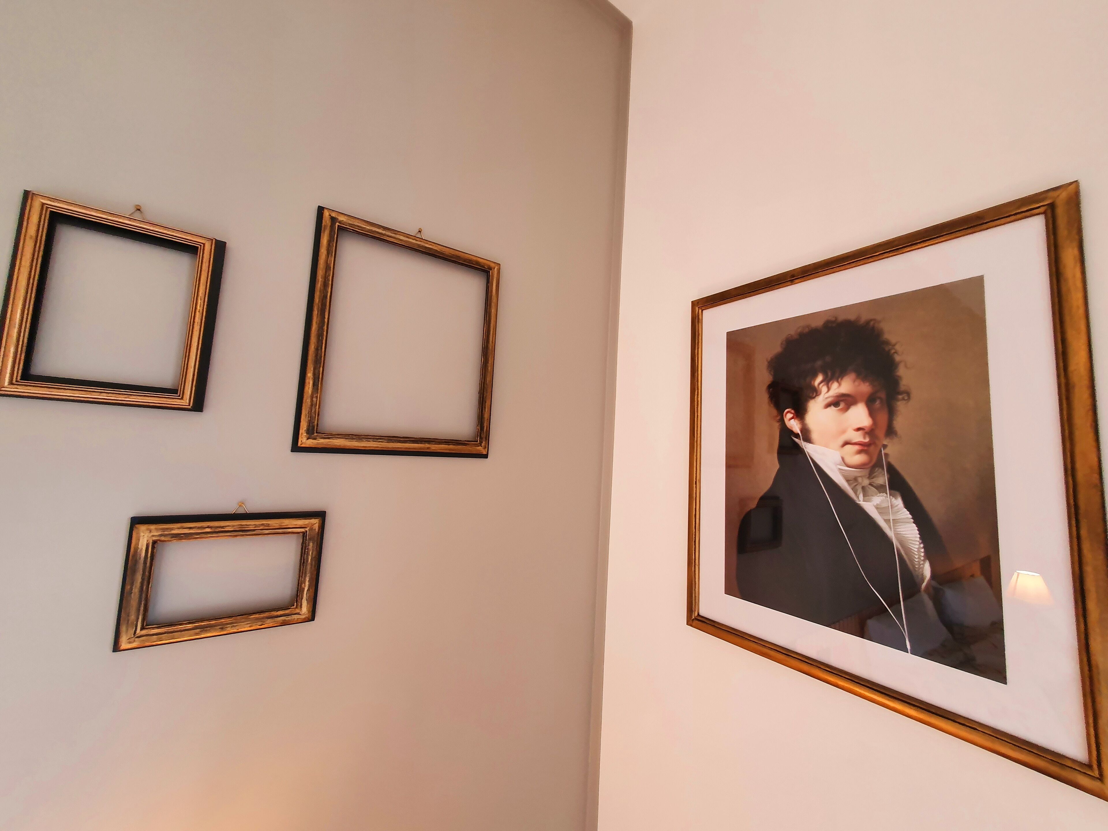 Een muur met vier ingelijste foto's, een groter portret en drie kleinere fotolijstjes.