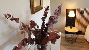 A room with a vase of purple leaves on a white table, a wooden-framed mirror on the wall, and a lamp with a wooden base on a small round table. - The calm, the charm, the Maison du Menez: "the place to be" (La Forêt-Fouesnant)