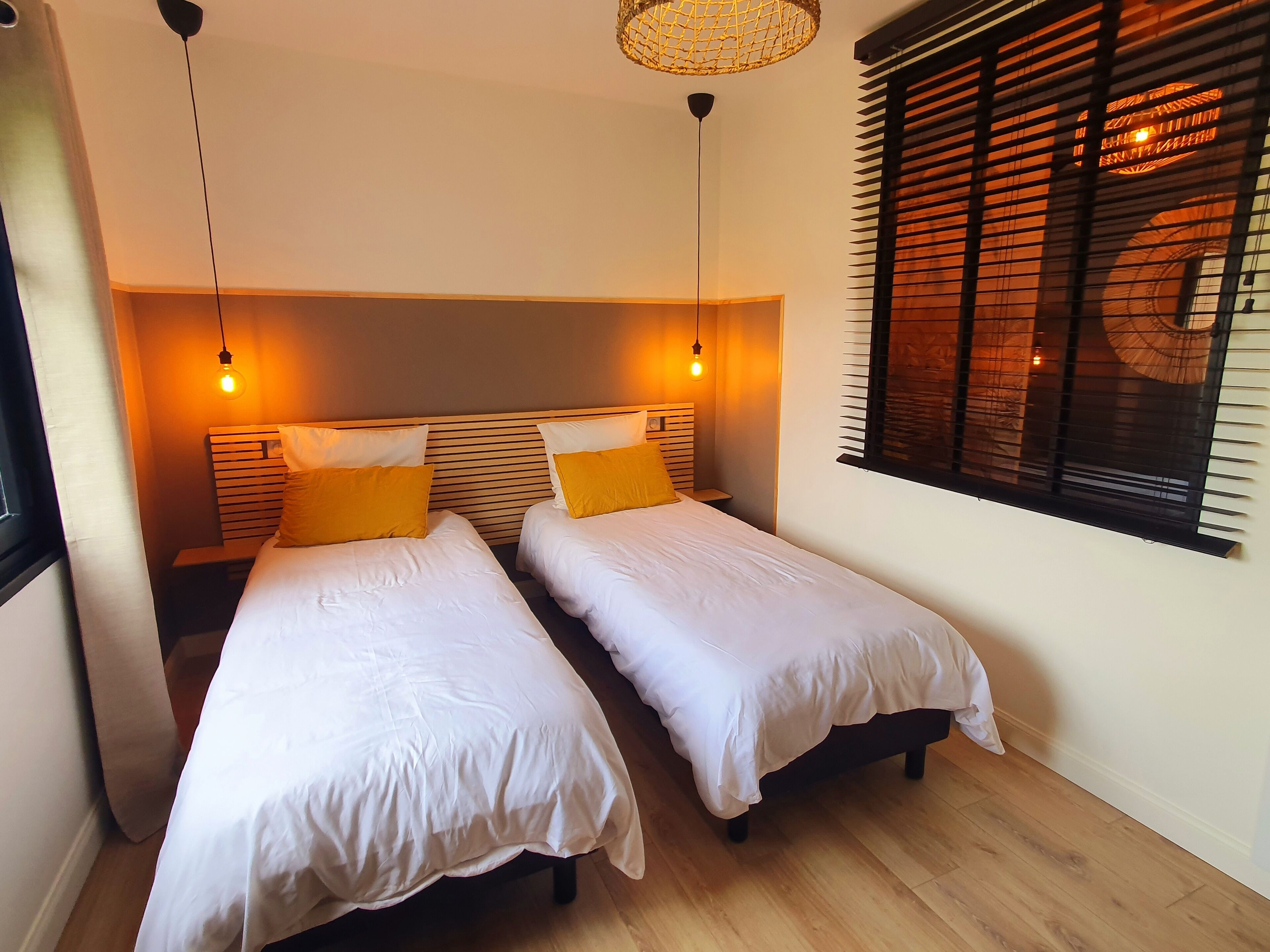 A bedroom with two single beds, wooden headboards, and a large window with blinds.
