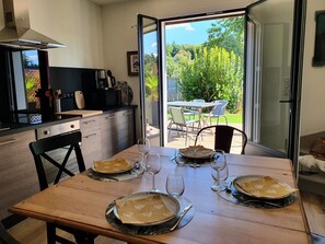Een eetgedeelte met een tafel voor vier personen, een keuken op de achtergrond en uitzicht op een tuin door een glazen deur.