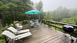 A wooden deck with outdoor furniture, a barbecue grill, and a blue umbrella.
