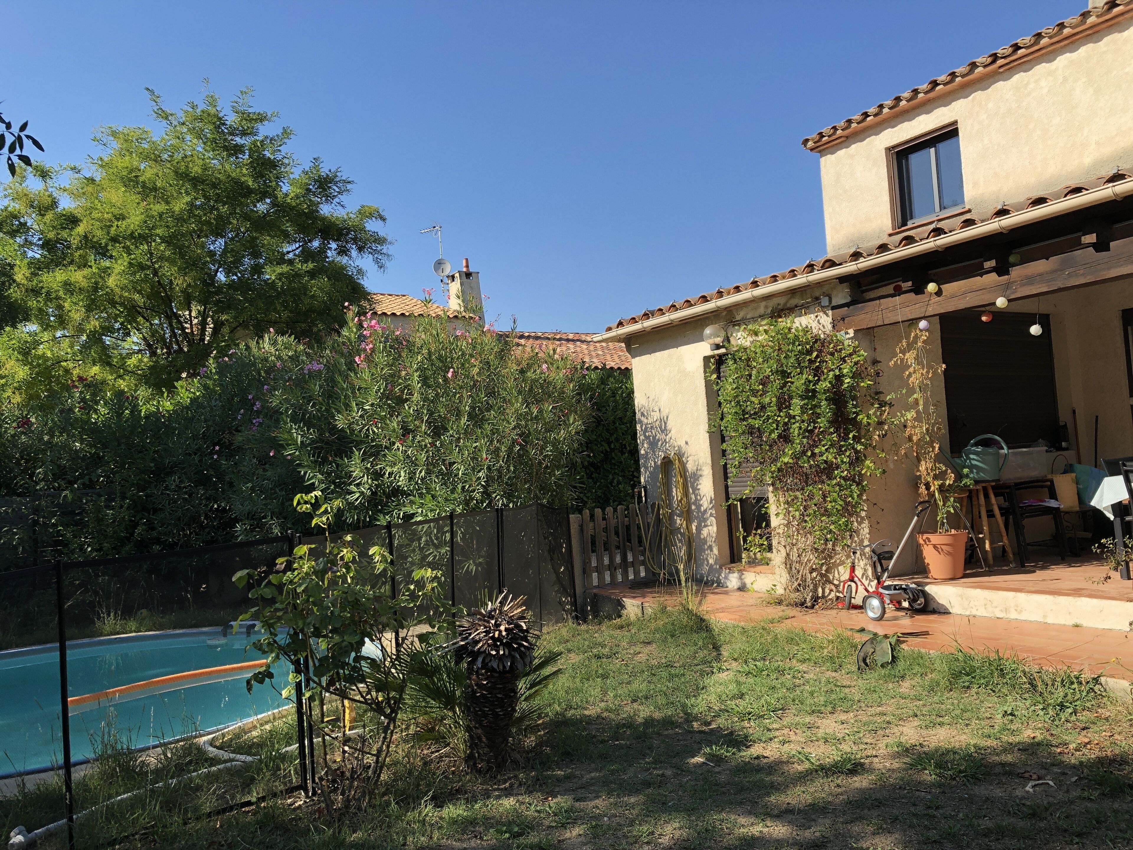 Un patio trasero residencial con piscina, zona de patio y una casa de techo de tejas y paredes de estuco.