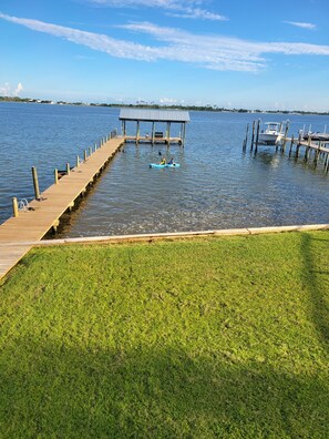 Un muelle de madera que se adentra en un cuerpo de agua tranquilo, con un área verde en primer plano.