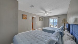 A bedroom with two beds, a ceiling fan, and a view of the outdoors.