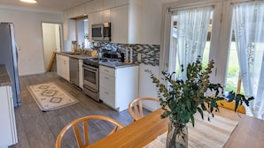 A modern kitchen with white cabinets, a microwave, and a gas stove. There is a dining table with chairs and a vase with flowers. - Green Door Getaway — family-friendly 4BR, 10 minutes to New River Gorge (Oak Hill)