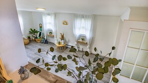 A spacious living room with a high ceiling, large windows with sheer curtains, and a variety of plants and decorative items. - Green Door Getaway — family-friendly 4BR, 10 minutes to New River Gorge (Oak Hill)
