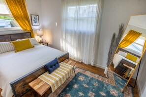A neatly arranged bedroom with a large bed, bedside tables, a mirror, and a window with curtains.