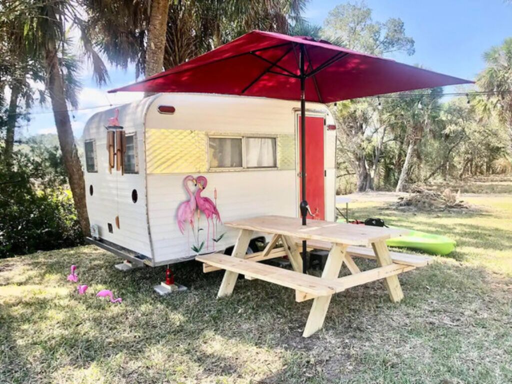 Uma caravana vintage com uma mesa de piquenique e um guarda-sol vermelho.