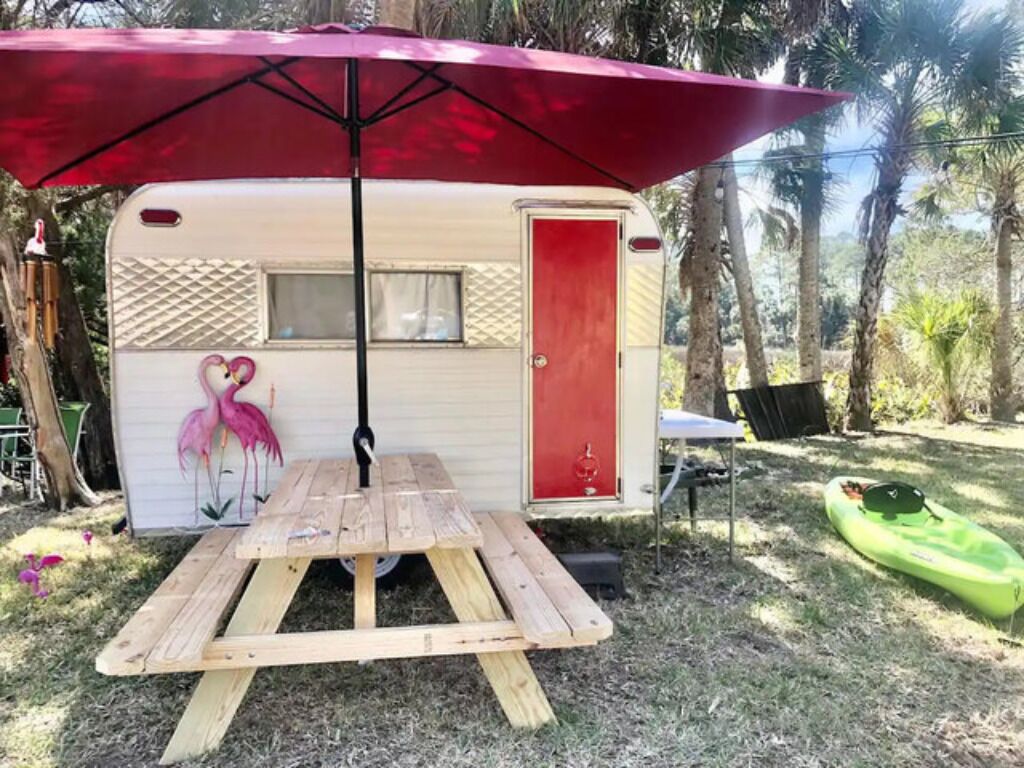 A mobile home with a red door, a picnic table, and a kayak nearby.