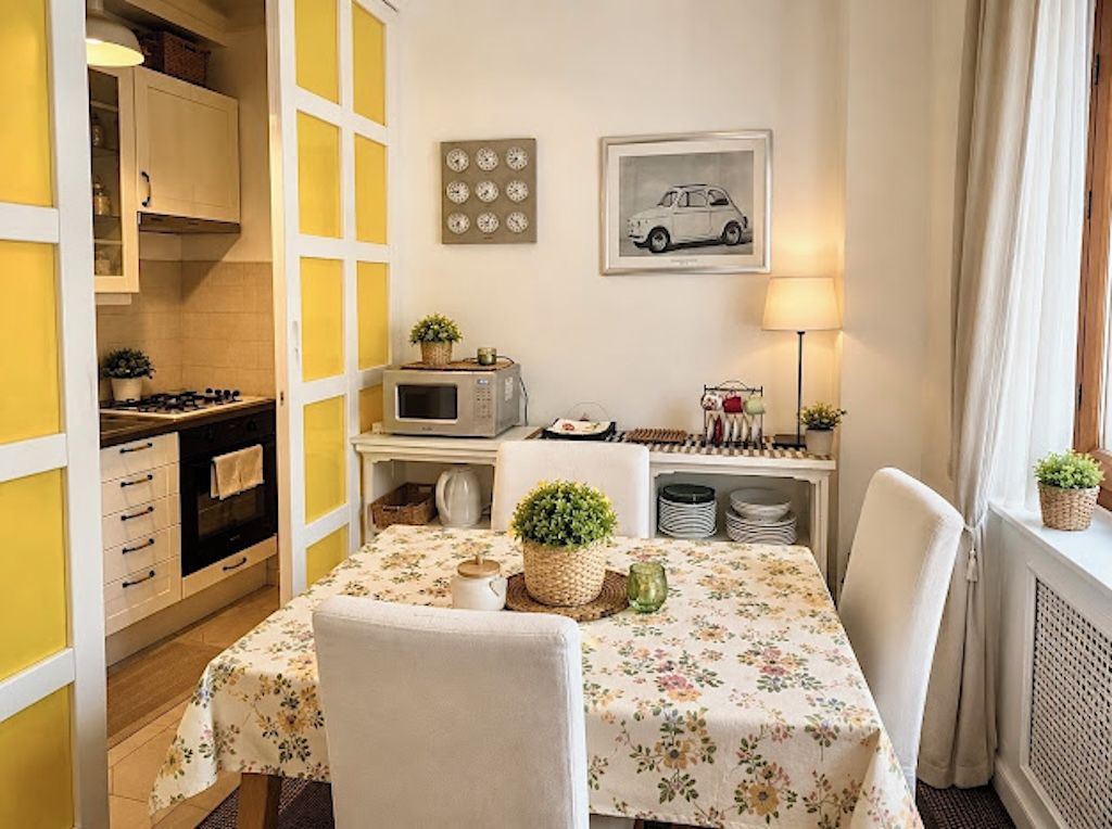 A compact kitchen with a microwave, stove, and cabinets. There is a dining table with chairs and a floral tablecloth.