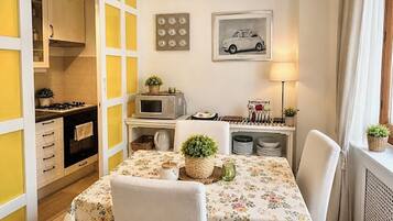 A compact kitchen with a microwave, stove, and cabinets. There is a dining table with chairs and a floral tablecloth.