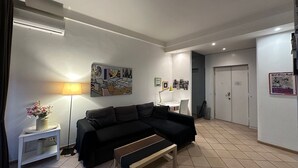 Een moderne woonkamer met een zwarte bank, een houten bankje, een vloerlamp en een schilderij aan de muur.