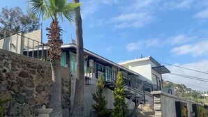Un edificio moderno con pared de piedra, palmeras y una escalera de hormigón que lleva a un balcón.