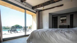 A bedroom with a large bed, a built-in wardrobe, and a sliding glass door leading to a pool area. - Mas des Pêcheurs (Le Ségur)