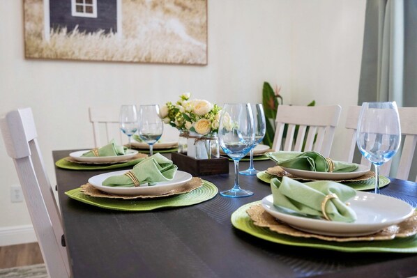 A dining table set with green placemats, white plates, and blue wine glasses.