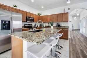 A modern kitchen with granite countertops, stainless steel appliances, wooden cabinets, and bar stools.
