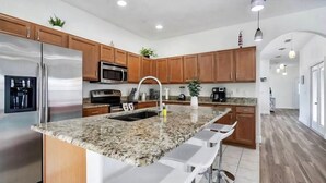 A modern kitchen with granite countertops, stainless steel appliances, wooden cabinets, and bar stools.