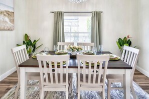 Un comedor con una mesa de madera oscura, sillas blancas y una ventana con cortinas.