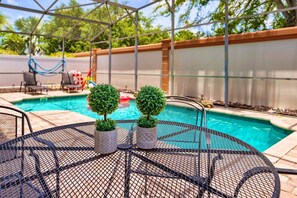 Un área de piscina con una mesa redonda y dos plantas en macetas.
