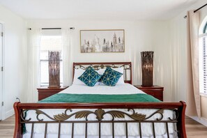 A neatly made bed with a green bedspread, two decorative pillows, and a cityscape painting above it.
