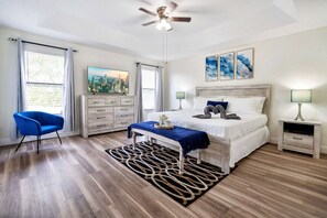 Un dormitorio con cama, escritorio, silla, ventilador de techo y obras de arte en la pared.