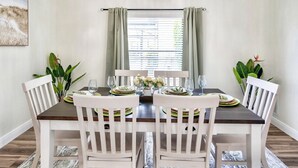 A dining area with a dark wooden table, white chairs, and a window with curtains.
