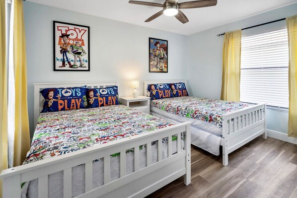 Un dormitorio con dos camas, cada una con una colcha temática de 'Toy Story', un ventilador de techo y dos carteles en la pared.