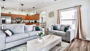 A modern living room with two grey sofas, a wooden coffee table, and a kitchen in the background.
