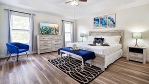 A bedroom with a bed, a desk, a chair, a ceiling fan, and artwork on the wall.