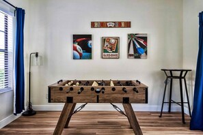 Una habitación con una mesa de fútbolín de madera, una lámpara y obras de arte que representan billares y salas de juegos.