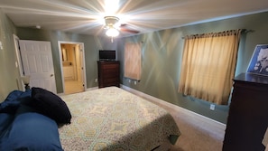 Un dormitorio con cama, cómoda, ventilador de techo y puerta que da a un baño.
