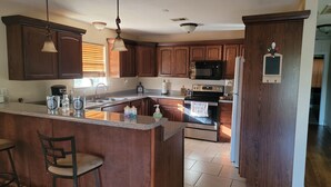 A kitchen with wooden cabinets, a granite countertop, a microwave, an oven, and a refrigerator. - J & S's Pond Da Rosa  A Place Apart From The Rest (Bay St. Louis)