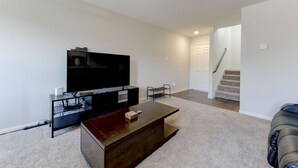 A living room with a flat-screen TV on a stand, a coffee table, and a staircase leading to another room. - Jarrell Jewel 💎 (Jarrell)