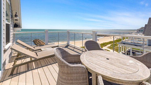 Terraza de madera con sillas de mimbre y una mesa con vista a la playa.