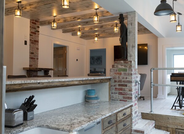 A kitchen with granite countertops, a brick accent wall, hanging pendant lights, and a statue.