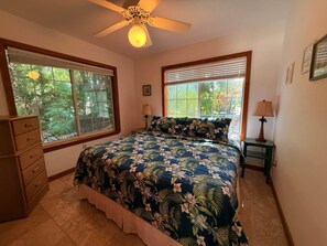 A bedroom with a bed, two nightstands, a ceiling fan, and large windows.