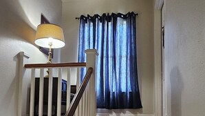 A staircase with wooden steps and white railings, leading to a room with a ceiling light and a window with blue curtains.