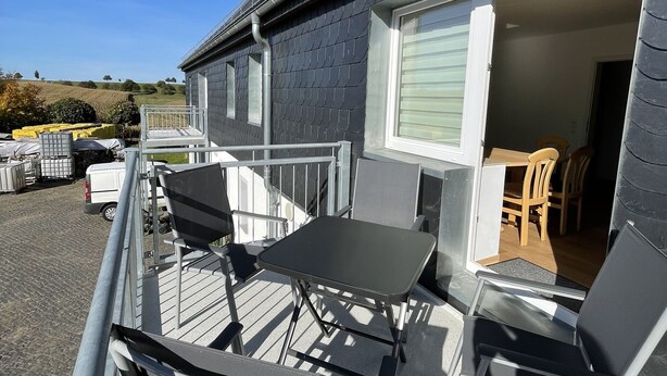 A balcony with a table and chairs, a covered outdoor area, and a building with a window and door. - Vacation apartment in the heart of Saxony (Leisnig)
