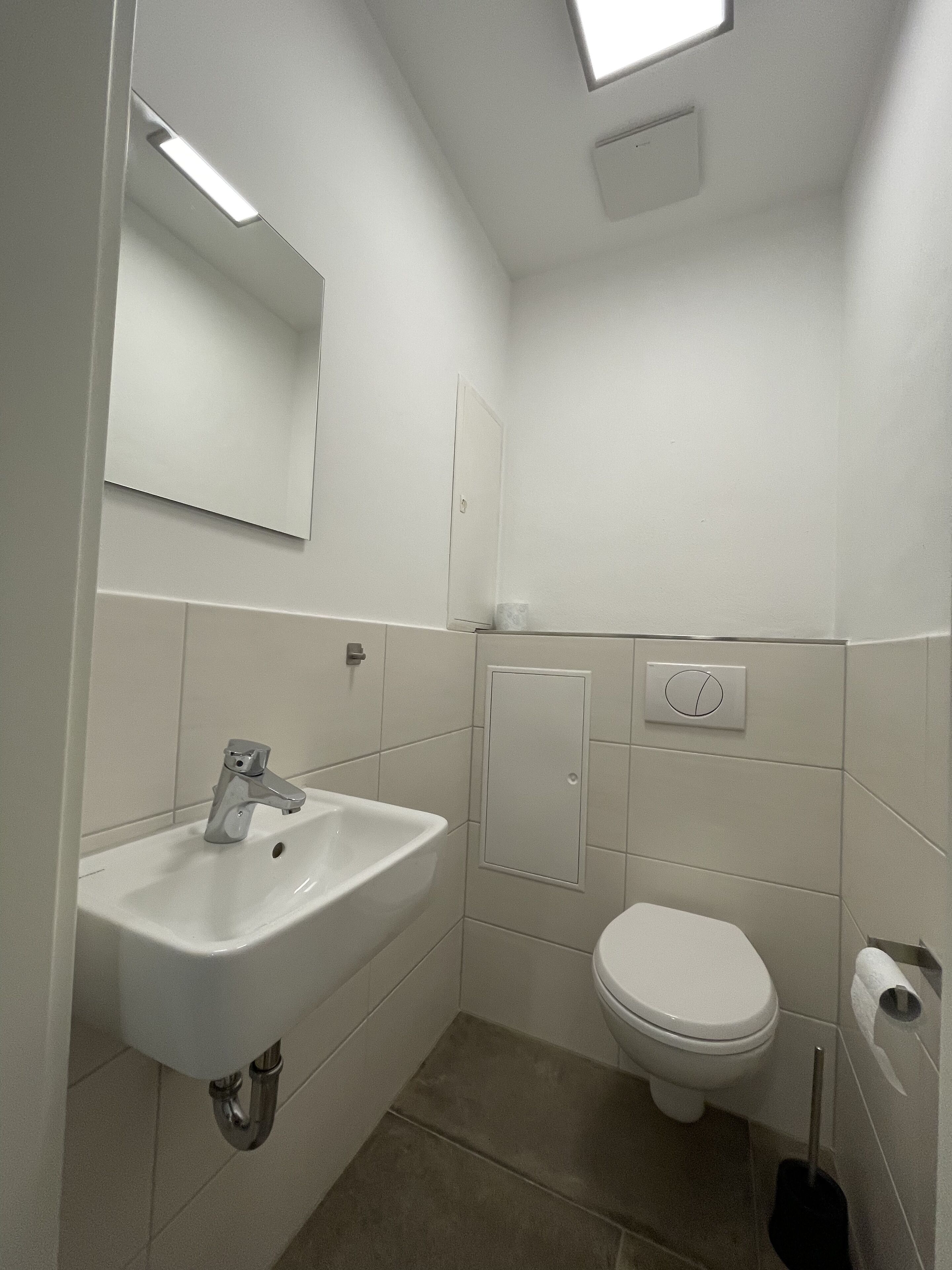 A modern bathroom with a white sink, a toilet, and a mirror.