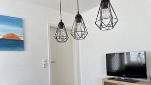 A modern living room with a flat-screen TV on a wooden cabinet, a sofa, and a painting of a sunset. - Vacation apartment in the heart of Saxony (Leisnig)