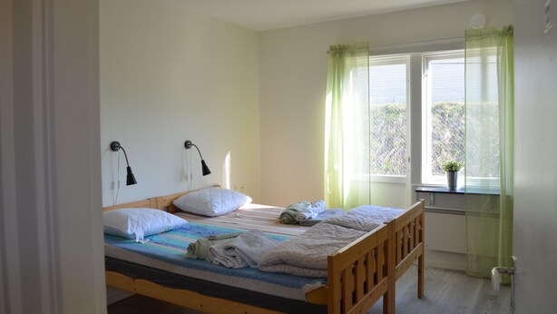 Een enkel bed met houten frame, twee bedlampen, een raam met dunne gordijnen en een kleine potplant op de vensterbank.