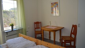 Een slaapkamer met een bed, een raam met gordijn, een tafel met stoelen en een lijst met een afbeelding aan de muur.