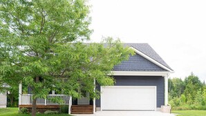 Une maison de plain-pied à l’extérieur bleu foncé, avec une porte de garage blanche et un porche à l’avant doté d’une balustrade en bois.
