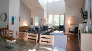 Un vaste espace de vie comprenant un canapé, des chaises en bois, une table en verre et un coin cuisine avec une cuisinière.