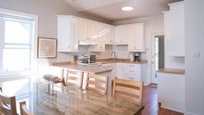 Une cuisine moderne avec des meubles blancs, une table à manger en bois et un lustre.